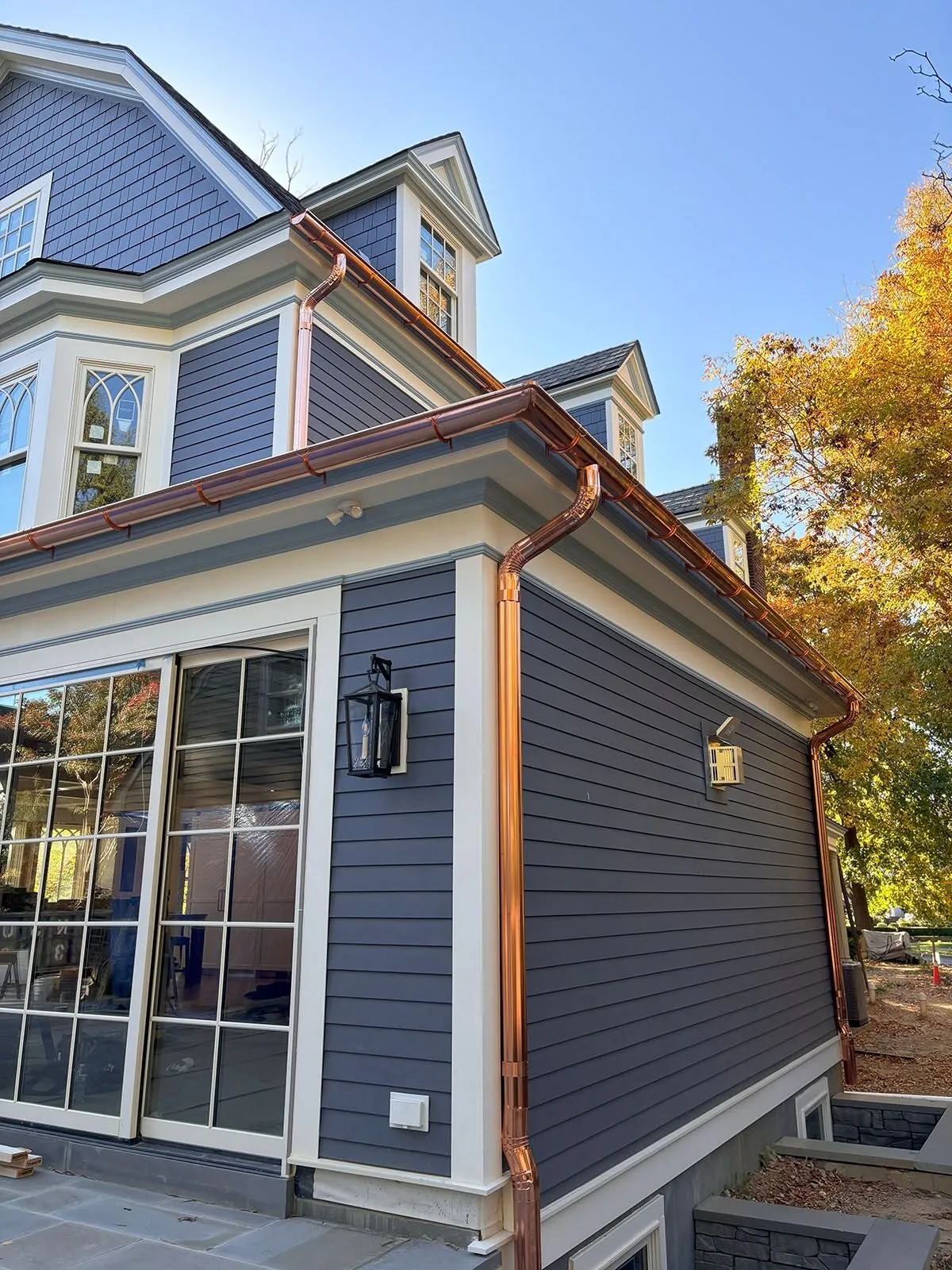Copper gutters and downspouts running down a blue-sided home